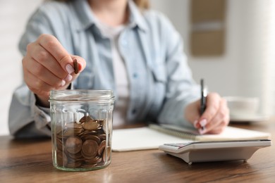 Photo of Woman counting and putting coins into jar at wooden table, selective focus