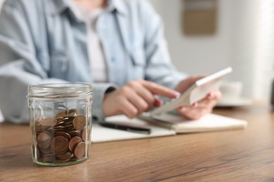 Photo of Woman counting and putting coins into jar at wooden table, selective focus