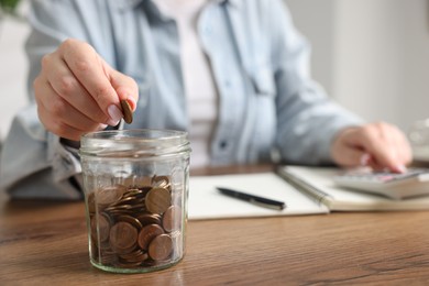 Photo of Woman counting and putting coins into jar at wooden table, selective focus