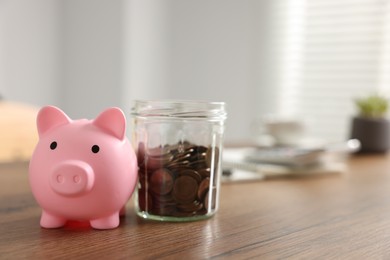 Photo of Piggybank and jar with coins on wooden table. Space for text