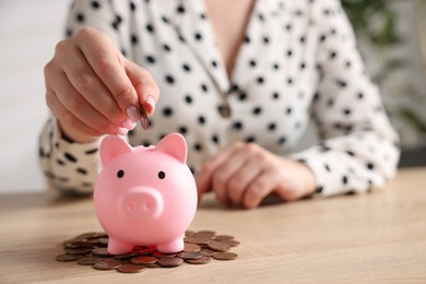 Photo of Woman putting money into piggybank at wooden table, closeup