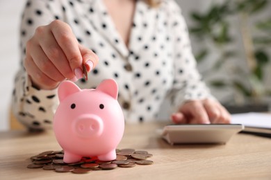 Photo of Woman counting and putting money into piggybank at wooden table, closeup