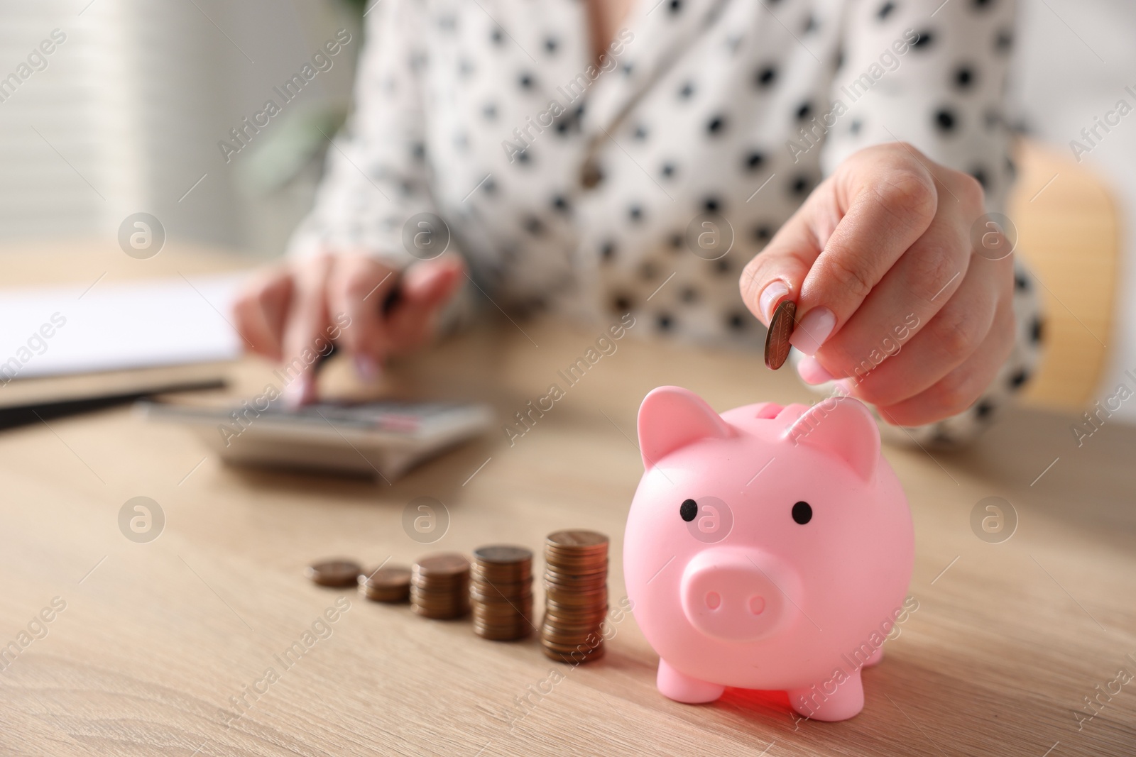 Photo of Woman counting and putting money into piggybank at wooden table, closeup