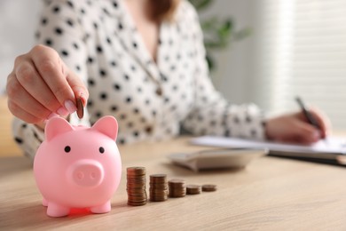 Photo of Woman planning budget and putting money into piggybank at wooden table, selective focus