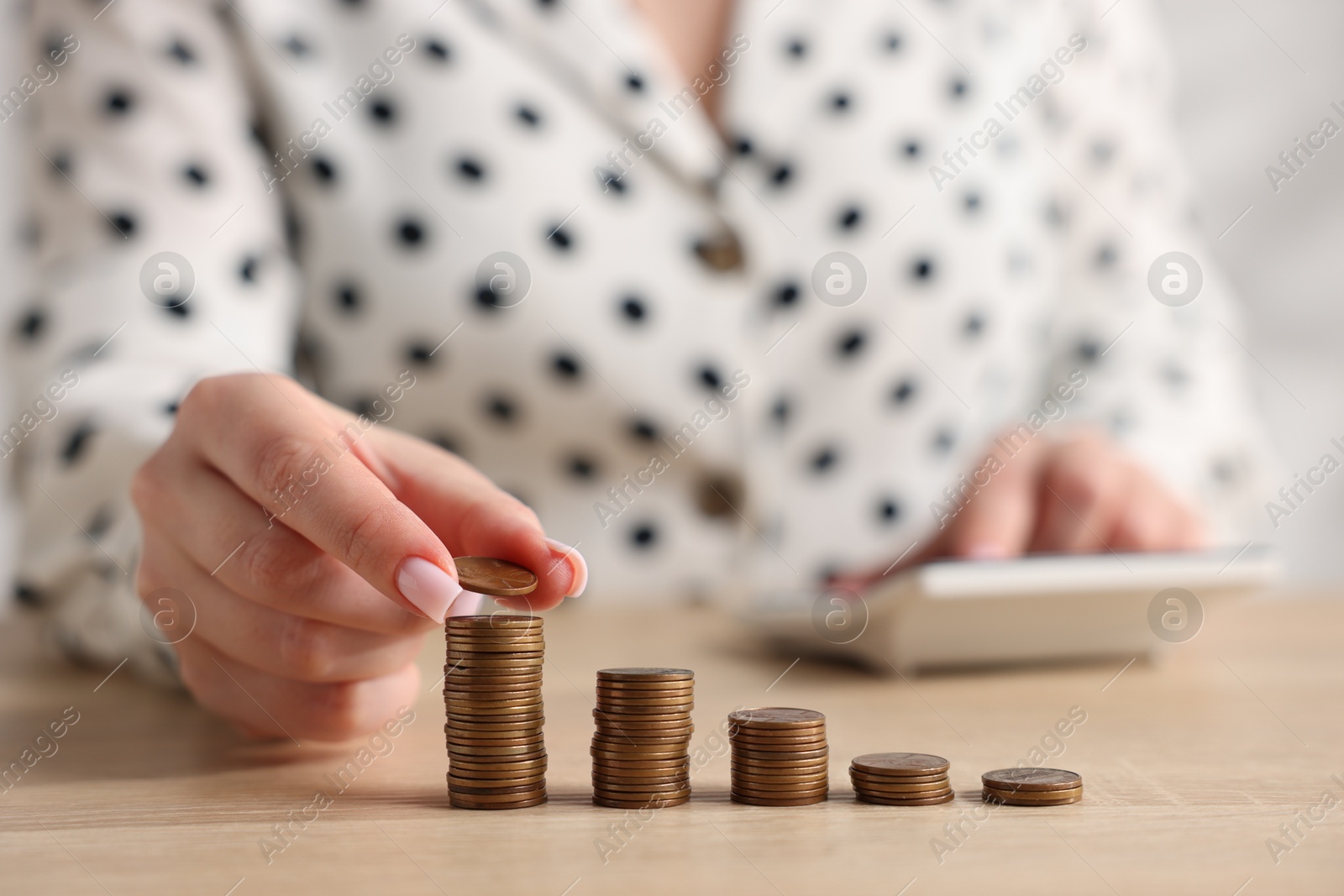 Woman with stacked coins and calculator at wooden table, closeup Photo of Woman with stacked coins and calculator at wooden table, closeup