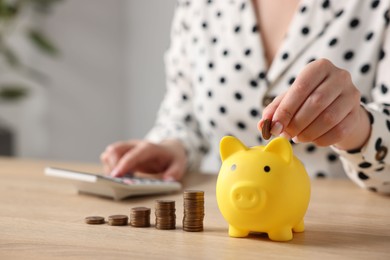 Photo of Woman counting and putting money into piggybank at wooden table, closeup