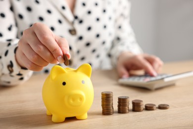 Photo of Woman counting and putting money into piggybank at wooden table, closeup