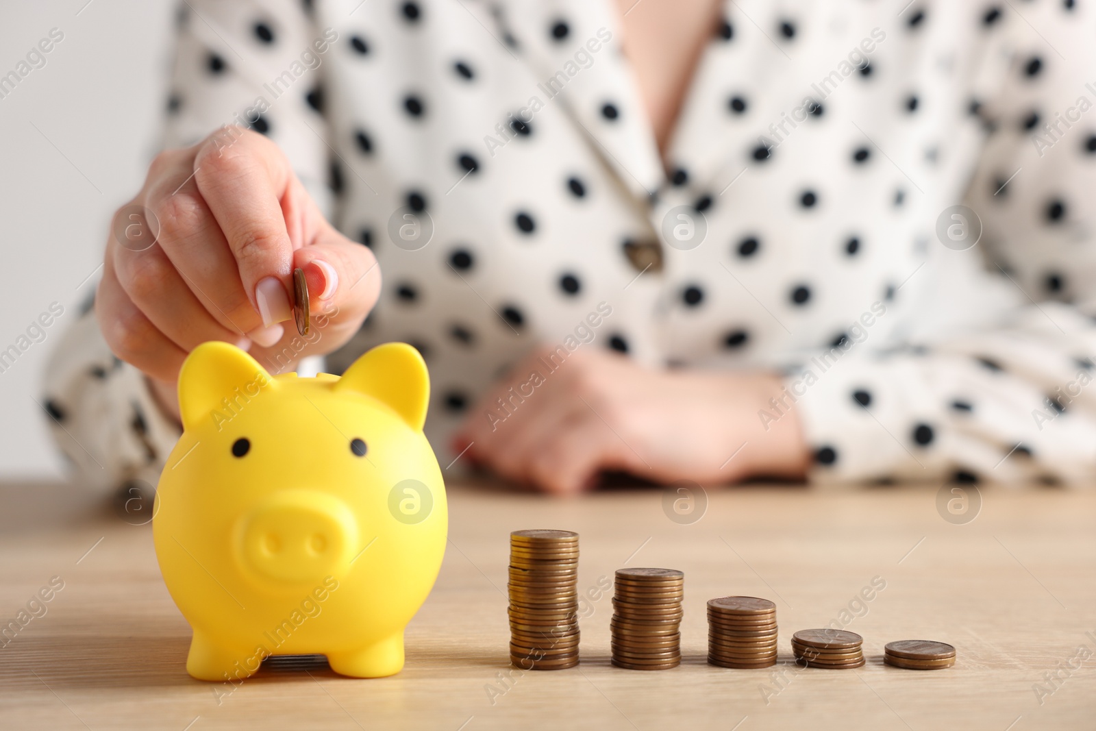 Woman putting money into piggybank at wooden table, closeup Photo of Woman putting money into piggybank at wooden table, closeup