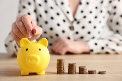 Photo of Woman putting money into piggybank at wooden table, closeup