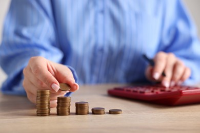Photo of Woman with stacked coins and calculator at wooden table, closeup