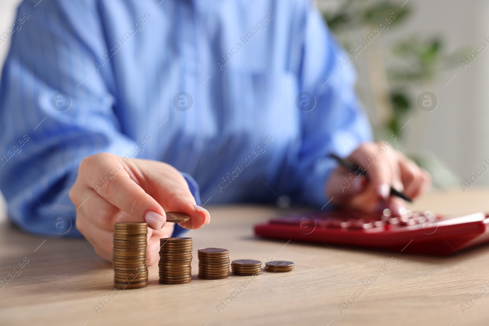 Woman with stacked coins and calculator at wooden table, closeup Photo of Woman with stacked coins and calculator at wooden table, closeup