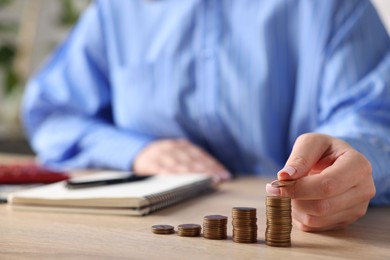 Photo of Woman stacking coins at wooden table, closeup