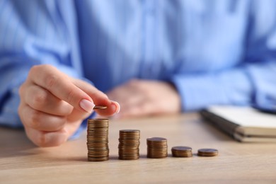 Photo of Woman stacking coins at wooden table, closeup