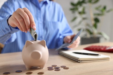 Photo of Woman putting money into piggybank at wooden table, closeup