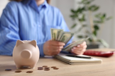 Photo of Piggybank with coins and woman counting money at wooden table, selective focus