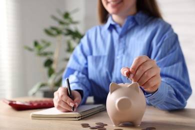 Photo of Woman planning budget and putting money into piggybank at wooden table, selective focus