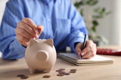 Photo of Woman planning budget and putting money into piggybank at wooden table, selective focus