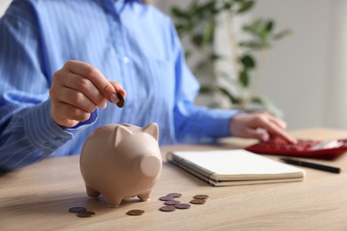 Photo of Woman counting and putting money into piggybank at wooden table, closeup