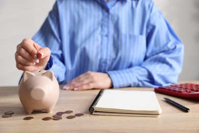Photo of Woman putting money into piggybank at wooden table, closeup