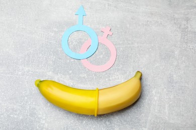 Photo of Sex education. Banana with condom and gender symbols on grey table, flat lay