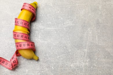 Photo of Sex education. Banana with condom and measuring tape on grey table, top view. Space for text