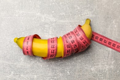 Photo of Sex education. Banana with condom and measuring tape on grey table, top view