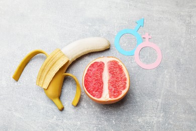 Photo of Sex education. Banana, half of grapefruit and gender symbols on grey table, flat lay