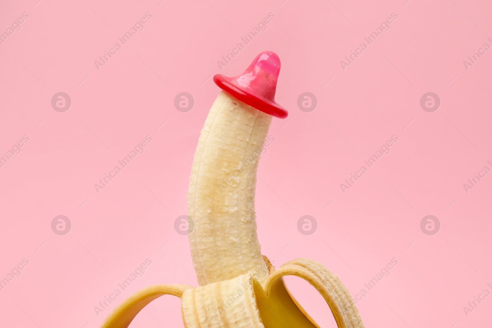 Photo of Sex education. Banana with condom on pink background, closeup