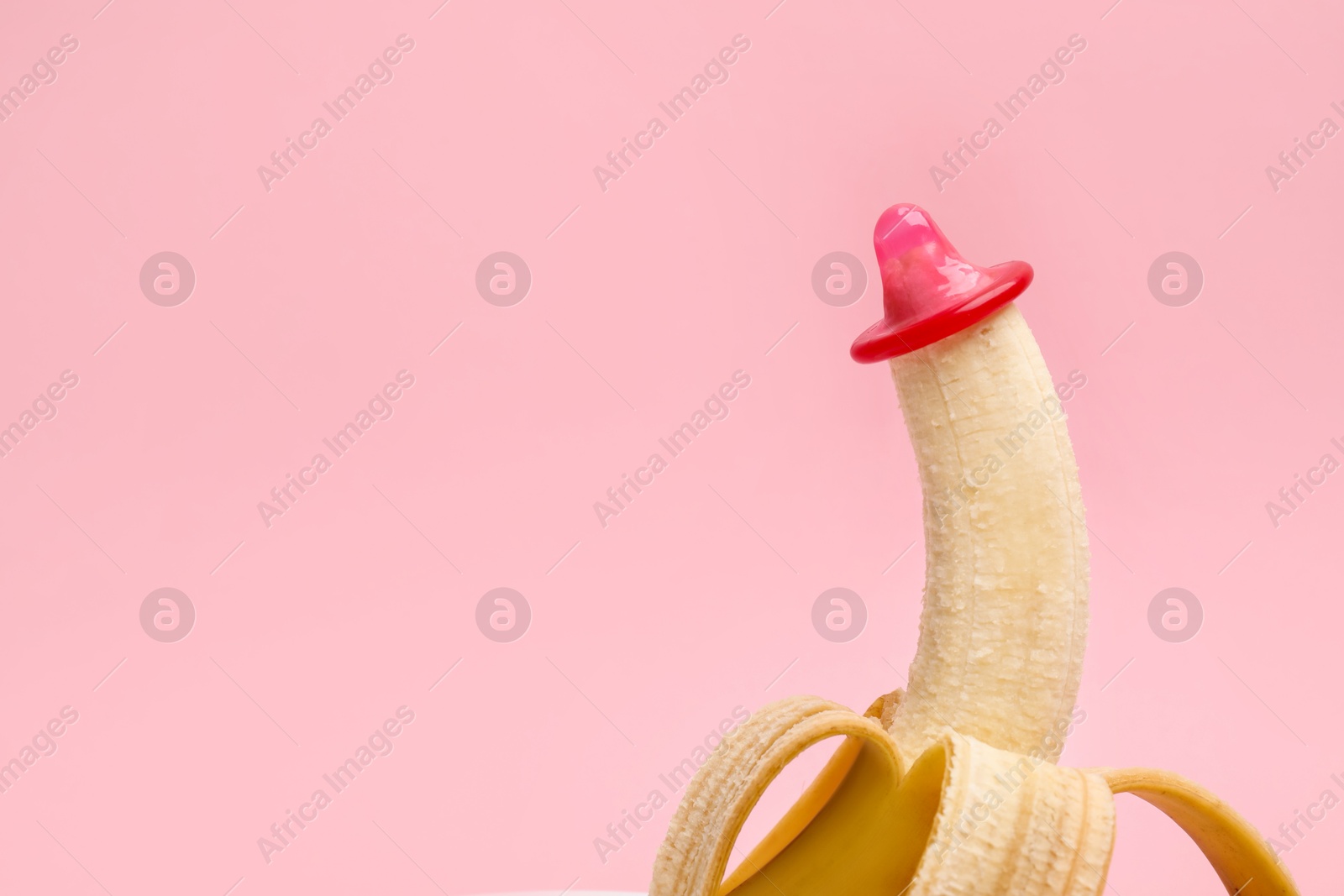 Photo of Sex education. Banana with condom on pink background, closeup. Space for text