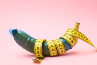 Photo of Sex education. Banana with condom and measuring tape on pink background, closeup