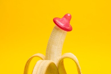 Photo of Sex education. Banana with condom on yellow background, closeup