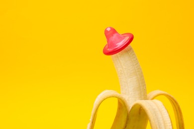 Photo of Sex education. Banana with condom on yellow background, closeup. Space for text