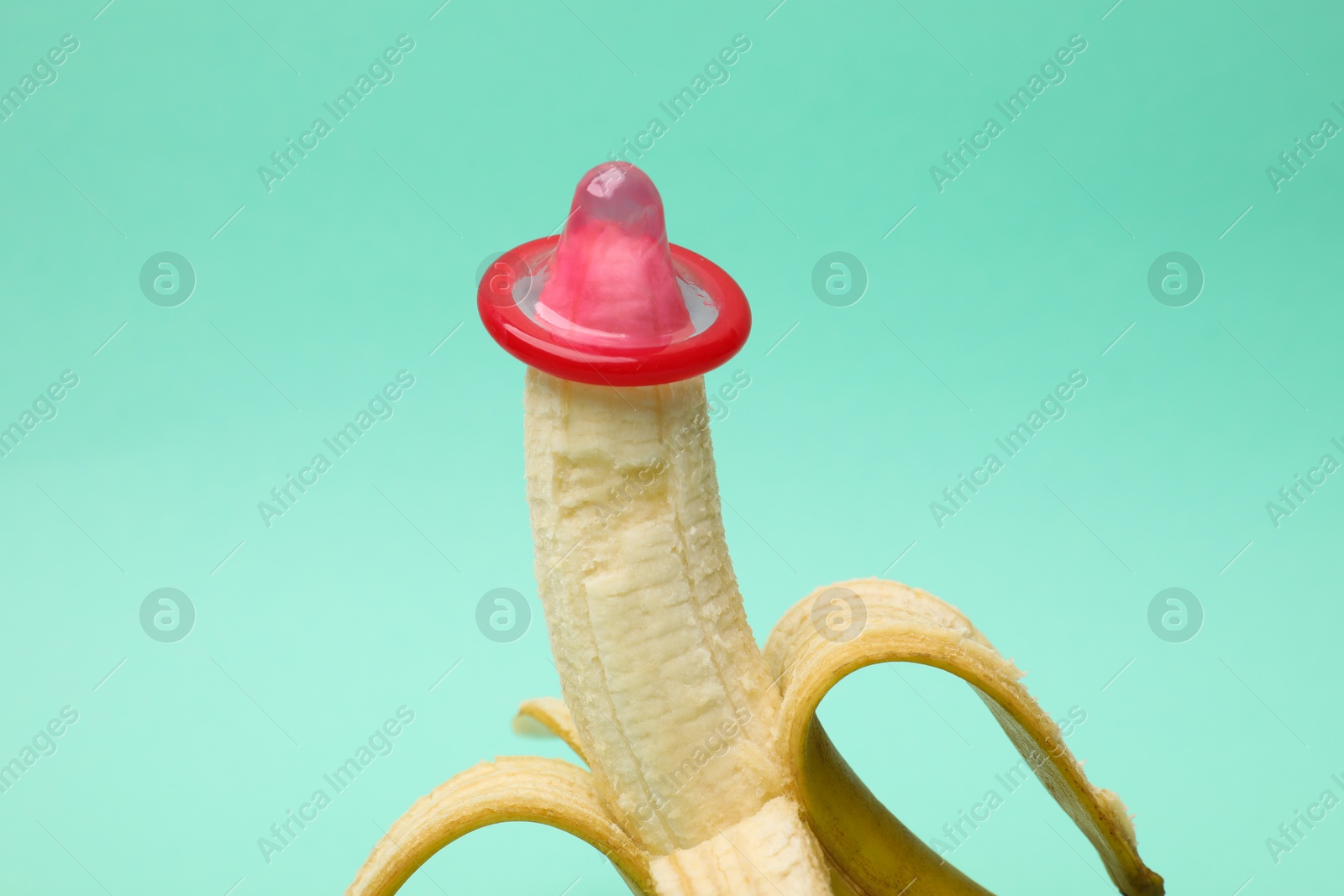 Photo of Sex education. Banana with condom on turquoise background, closeup