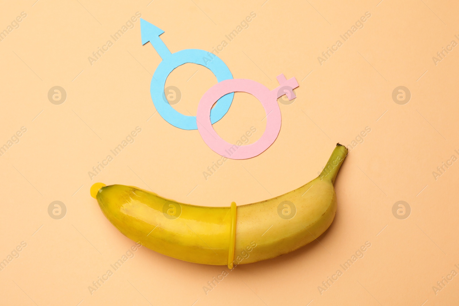 Photo of Sex education. Banana with condom and gender symbols on beige background, flat lay