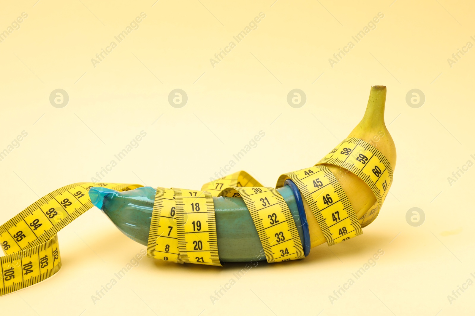 Photo of Sex education. Banana with condom and measuring tape on beige background