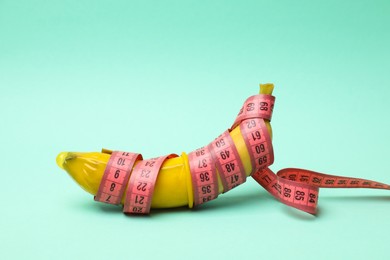 Photo of Sex education. Banana with condom and measuring tape on turquoise background