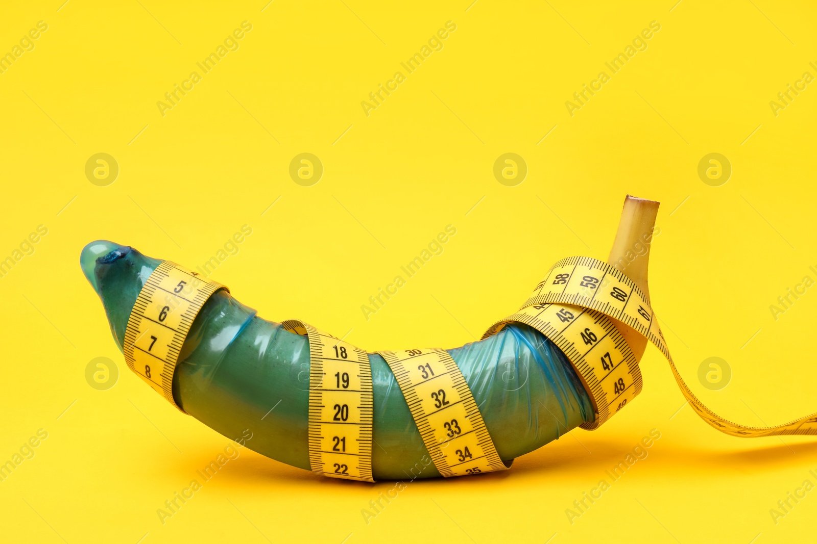 Photo of Sex education. Banana with condom and measuring tape on yellow background