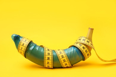 Photo of Sex education. Banana with condom and measuring tape on yellow background
