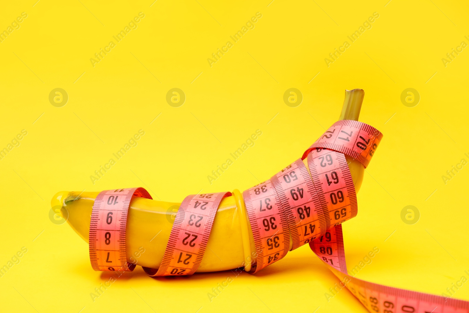 Photo of Sex education. Banana with condom and measuring tape on yellow background