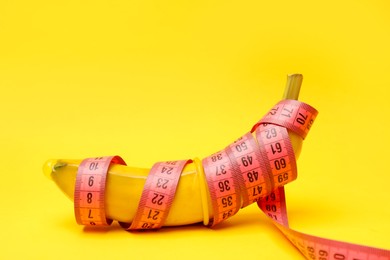 Photo of Sex education. Banana with condom and measuring tape on yellow background