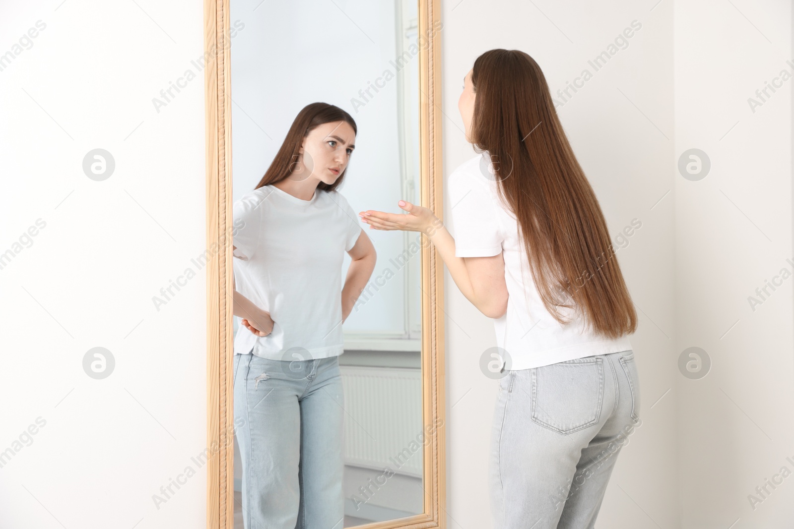 Image of Excited woman looking at irritated reflection of herself in mirror indoors. Suppressed emotions