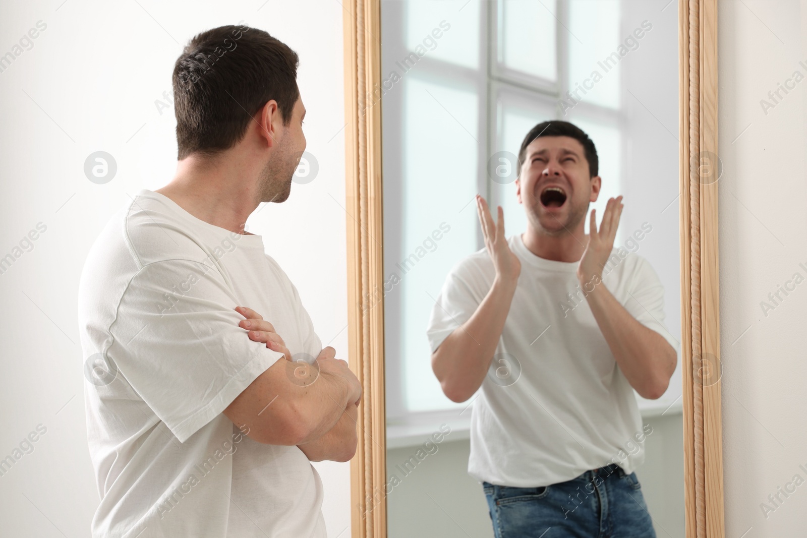 Image of Man looking at screaming reflection of himself in mirror indoors. Suppressed emotions