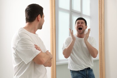 Image of Man looking at screaming reflection of himself in mirror indoors. Suppressed emotions