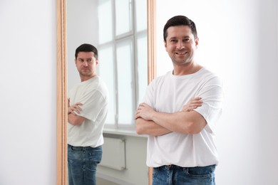 Image of Happy man near mirror with serious reflection of himself indoors. Mental health