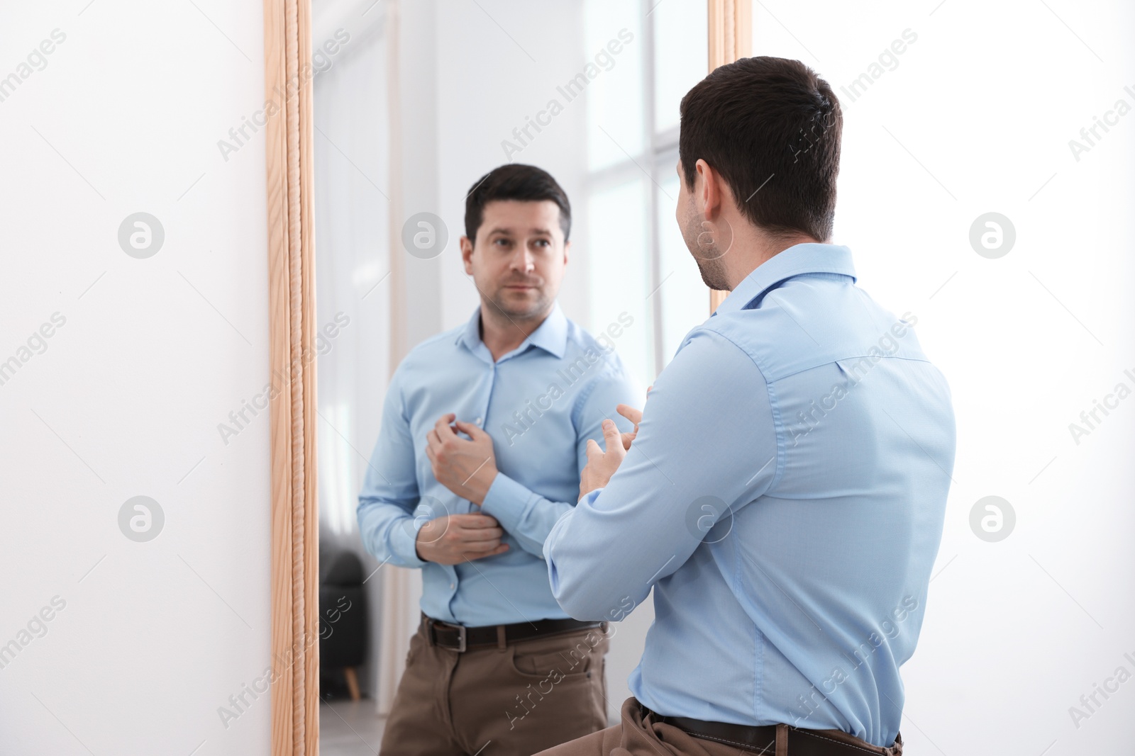 Image of Man looking at serious reflection of himself in mirror indoors. Mental health