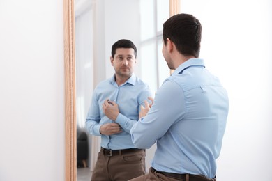 Image of Man looking at serious reflection of himself in mirror indoors. Mental health