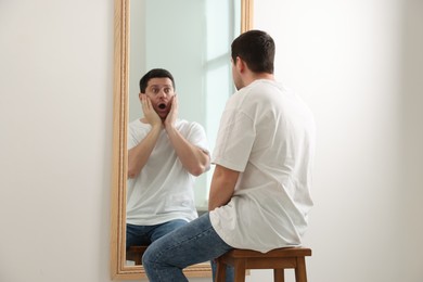 Image of Man looking at shocked reflection of himself in mirror indoors. Mental health