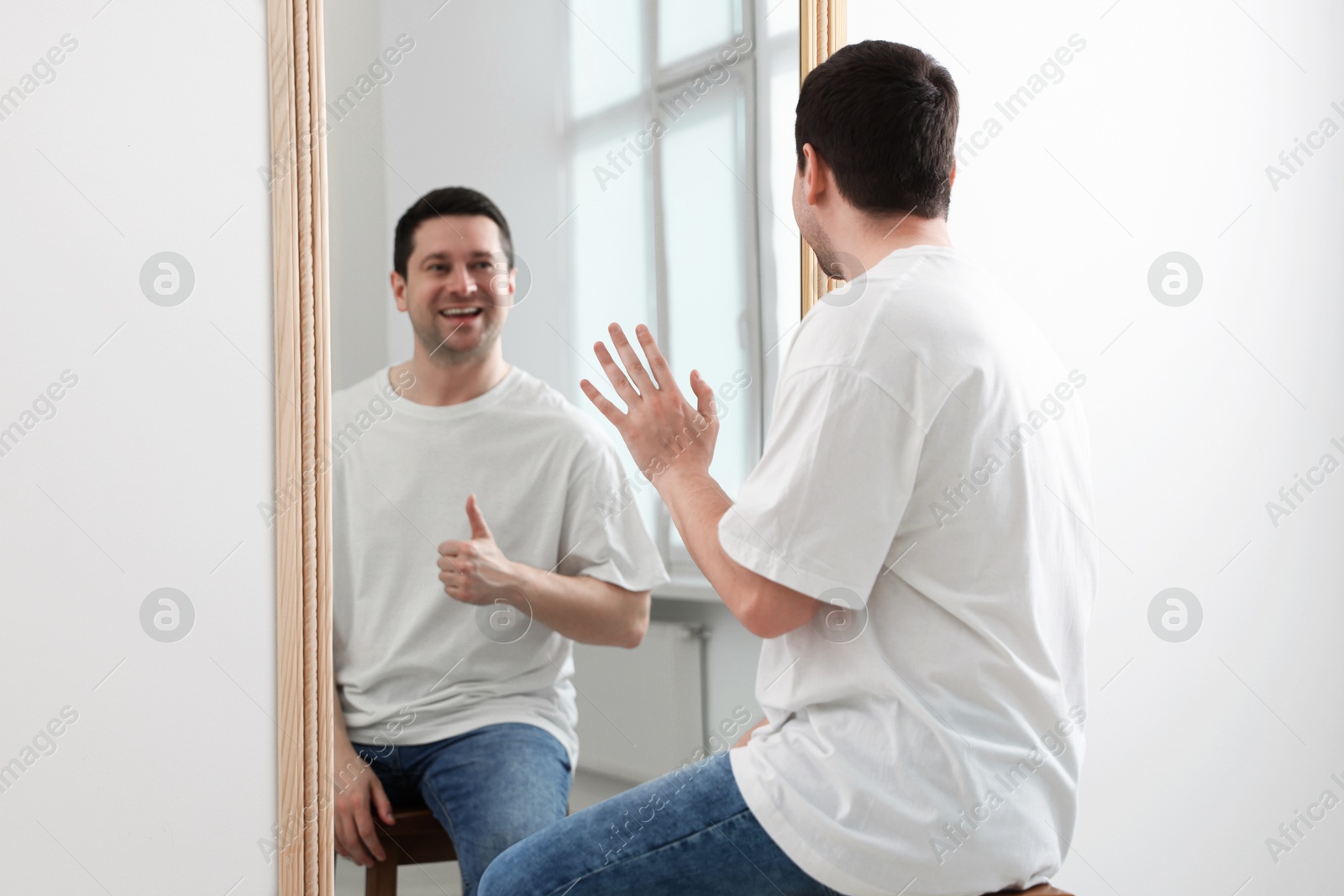 Image of Man sitting in front of mirror where his reflection showing thumbs up indoors. Mental health