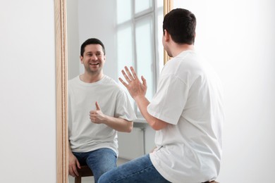 Image of Man sitting in front of mirror where his reflection showing thumbs up indoors. Mental health