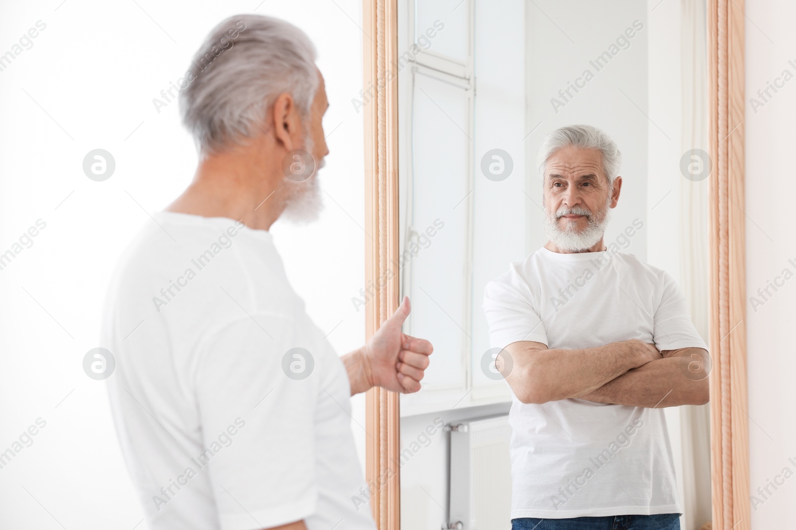 Image of Senior man showing thumbs up to his confident reflection indoors. Mental health